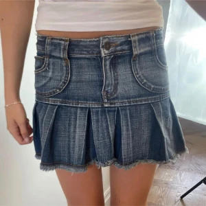 Lowwaist jeanskjol - En kort jeanskjol med veck och fickor fram och bak. Kjolen har en knapp och dragkedja framtill samt bälteshällor. Väldigt bra skick!