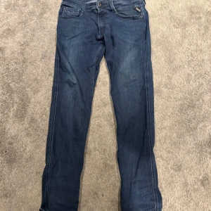 Blå jeans från Replay - Snygga blå jeans från Replay med klassisk femficksdesign och knappgylf. Perfekta för en avslappnad stil. Märkesdetaljer syns på bakfickorna och vid linningen.