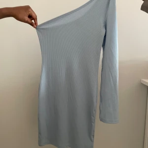 Ljusblå oneshoulder klänning - Snygg ljusblå oneshoulder klänning med en slit på armen med ribbad struktur. Perfekt för en stilren look. Klänningen har långa ärmar och en smickrande passform.