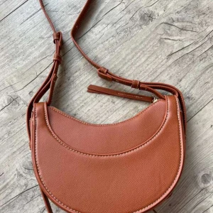 Brun axelväska i syntet - Snygg brun axelväska i syntetmaterial med en stilren design. Väskan har en justerbar axelrem och en praktisk dragkedja upptill. Perfekt för att bära med sig det viktigaste på ett trendigt sätt.