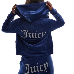 Blå juicy set från Juicy Couture  - Snyggt blått set från Juicy Couture med glittrande text på ryggen och rumpan. Överdelen har en huva och långa ärmar, perfekt för en avslappnad stil. Matcha med de tillhörande byxorna för en komplett look.
