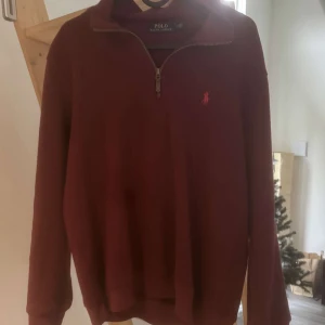 Vinröd tröja från Polo Ralph Lauren - Säljer en stilren vinröd tröja från Polo Ralph Lauren med dragkedja vid halsen. Tröjan har en broderad logotyp på bröstet och långa ärmar. Perfekt för en avslappnad och snygg look.