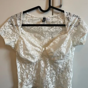 Vit spetsblus - Säljer en söt vit spetsblus från hm med korta ärmar och en vacker knytdetalj framtill. Perfekt för sommarens varma dagar eller en festlig kväll. Blusen har en romantisk och feminin stil.