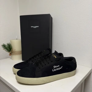 Svarta sneakers från Saint Laurent - Snygga svarta sneakers från Saint Laurent med vit logga på sidan. Skorna har en klassisk design med snörning och en ljus sula som kontrasterar mot det svarta tyget. Ps använda ca 3-6 gånger. Kvitto finns i dm