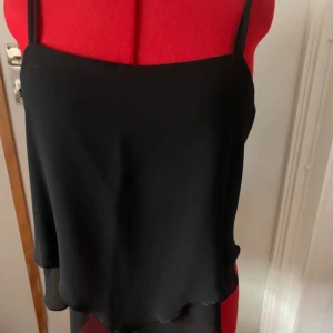 Svart linnetopp från Almia - Snygg svart linnetopp från Almia med smala axelband. Perfekt för en stilren look. Toppen har en enkel och elegant design som passar till många olika outfits.