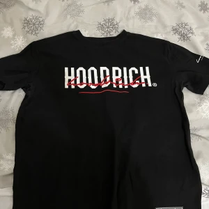 Svart t-shirt från Hoodrich - Snygg svart t-shirt från Hoodrich med vit och röd logga på bröstet. Perfekt för en casual look. Kortärmad och tillverkad i mjukt material för extra komfort. Pris kan diskuteras!!