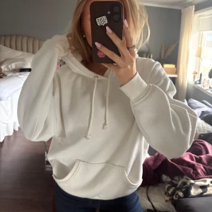 Vit hoodie med ficka - Säljer en vit hoodie med en stor ficka framtill och justerbar dragsko i huvan. Perfekt för en avslappnad look. Passar bra till jeans eller leggings. Lite smått nopprig