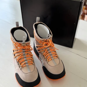 Inuiki Kebenelaise - Beige och orange boots med snörning - Helt nya i kartong. Snygga boots i beige med orange detaljer och snörning. Skorna har en robust vibramsula med orange mönster och svart förstärkning vid tån. Perfekta för svensk vinter. Nypris 4390 kr. Rea online nu för 2670. Mitt pris 1600