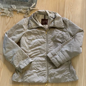 Beige jacka från Moncler - Säljer en stilren beige jacka från Moncler. Jackan har en dragkedja framtill och är tillverkad i 100% polyester med foder av polyamid. Perfekt för våren. 