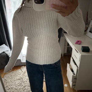 Vit ribbad tröja med knyt - Säljer en stilren vit ribbad tröja med långa ärmar och en snygg knytning i ryggen. Perfekt för att hålla sig varm och trendig. Passar bra till jeans eller kjol för en avslappnad look.
