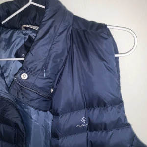 Lättviktsväst GANT - GANT väst i marinblå. Storlek M. Dragkedja, invändig ficka, två sidofickor och inbyggd luva som man man väckla ut.   Använd ca 1-2 gånger därav i princip nyskick. Enligt hemsidan nypris ca 2000-2500kr.Storlek medium men skulle säga är mer än s/m