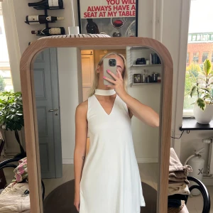 Vit ärmlös klänning - Säljer en stilren vit klänning med en chic hög krage. Klänningen är ärmlös och har en elegant A-linjeform som passar perfekt för sommarens alla fester. Den är gjord i ett lätt och bekvämt material, perfekt för varma dagar.