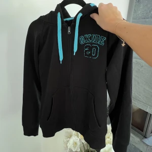 Svart hoodie - En svart hoodie med ljusblå detaljer i storlek L 🩵 Har blivit lite nopprig.   Längd: 60 cm