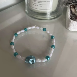 Armband med turkos dödskalle - Säljer ett coolt armband med vita pärlor och turkosa detaljer. Armbandet har en unik turkos dödskalle som ger det en edgy look. Perfekt för att piffa upp din outfit!