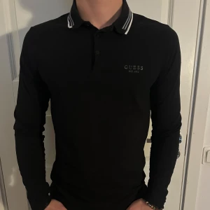 Svart pikétröja från Guess - En stilren svart pikétröja från Guess. Den har en klassisk krage och är extra slim fit i passform. Tröjan är i bra skick! Storlek M men passar även som S. Modellen är 182 cm och väger 75 kg. Pris går att diskuteras!