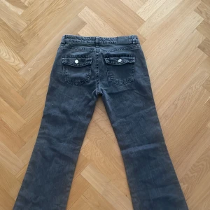 Grå bootcut jeans från Gina tricot - Säljer ett par snygga grå jeans från Perfect Jeans i storlek 36. De har en klassisk femficksdesign med knappar och dragkedja framtill. Jeansen har en bootcut passform och är perfekta för både vardag och fest. De är i bra skick och redo för en ny ägare!