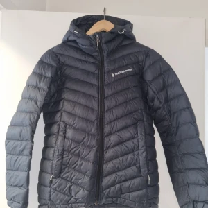 Svart dunjacka från Peak Performance - Säljer en snygg mörkblå dunjacka från Peak Performance. Jackan har en dragkedja framtill och en praktisk huva. Perfekt för kyliga dagar med sin design som håller värmen. Den är i mycket bra skick och passar perfekt för både höst och vinter. Stolek S för kvinnor. Använd fåtal gånger (max 5 gånger) 