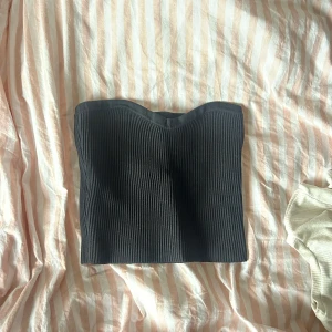 Svart ribbad tubtopp - Säljer en stilren svart ribbad tubtopp i nyskick. Perfekt för sommardagar eller som en basplagg under en kavaj. Den är stretchig och bekväm, vilket gör den idealisk för både vardag och fest. Passar bra till jeans eller kjol!