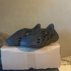 Svarta sandaler - Säljer ett par svarta sandaler i nyskick. De har en modern och luftig design med flera öppningar för bra ventilation. Perfekta för sommardagar eller som bekväma inneskor. Sulan är mönstrad för extra grepp.