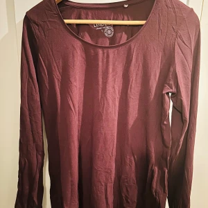Mörklila långärmad tröja från Lindex - Säljer en mörklila långärmad tröja från Lindex i ekologisk bomull. Perfekt för höst och vår, med en enkel och stilren design. Tröjan är mjuk och bekväm, idealisk för vardagsbruk. Passar bra till jeans eller kjol för en avslappnad look.