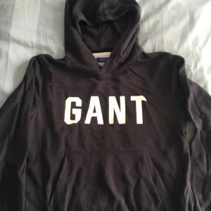 Svart hoodie från GANT - Säljer en snygg mörkblå hoodie från GANT i storlek 158/164 cm, perfekt för tonåringar. Den har en klassisk design med GANT-loggan i vitt på bröstet och en bekväm huva. 