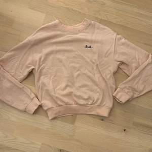 Rosa sweatshirt från HM - Mysig beige sweatshirt med broderad text 'Smile' på bröstet. Perfekt för en avslappnad stil. Tröjan har långa ärmar och en normal passform. Tröjan är i storlek xs och kommer från hm:s koncept ”divided”.