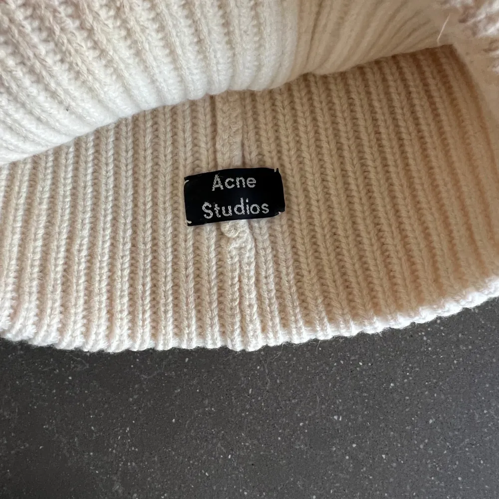 Säljer en superfin beige stickad mössa från Acne Studios. Den är ribbad och har en svart patch framtill som ger en cool touch. Perfekt för att hålla sig varm under höst och vinter. Mössan är i bra. skick och passar de flesta tack vare sin stretchiga design. Har lite sminkfläckar på insidan! . Accessoarer.