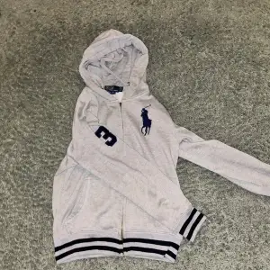 Säljer nu denna fina Ralph lauren zip hoodie i storlek S då den inte kommer till användning.                                              En bit av dragkedjan där man drar har gått av men den funkar fortfarande utan problem. Kan skicka bilder på den i dm. Tvivla inte på att höra av er vid funderingar!