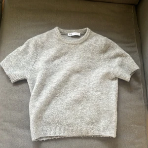 Grå tröja från Zara - Säljer en supermjuk och stilren grå tröja från Zara. Perfekt för både vardag och mysiga stunder. Tröjan har korta ärmar och en klassisk rund halsringning. Den är i ett skönt material som känns lyxigt mot huden. Passar perfekt till jeans eller kjol för en avslappnad look.