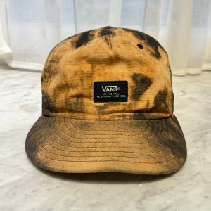 Tie-dye keps från Vans - Säljer en cool tie-dye keps från Vans i svart och orange. Kepsen har en justerbar rem baktill för perfekt passform och en broderad Vans-patch framtill.    🧢 Jag har flera kepsar till salu på min profil och lägger upp nya modeller regelbundet. 