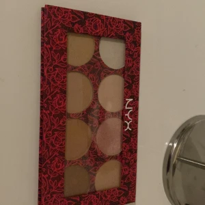 Glow Kit från NYX - Säljer en superfin Glow Kit från NYX med sex olika nyanser av highlighter. Perfekt för att få den där extra glöden! Paletten har en snygg röd och svart design med blommönster. Färgerna varierar från ljusa till gyllene toner, vilket gör den idealisk för både vardag och fest. Använd den för att framhäva kindben, näsrygg och amorbåge.