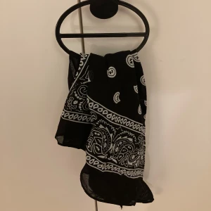 Svart och vit mönstrad bandana - Snygg svart bandana med vitt paisleymönster. Perfekt accessoar för att ge din outfit en cool touch. Passar både till vardags och fest. Materialet känns lätt och bekvämt mot huden.