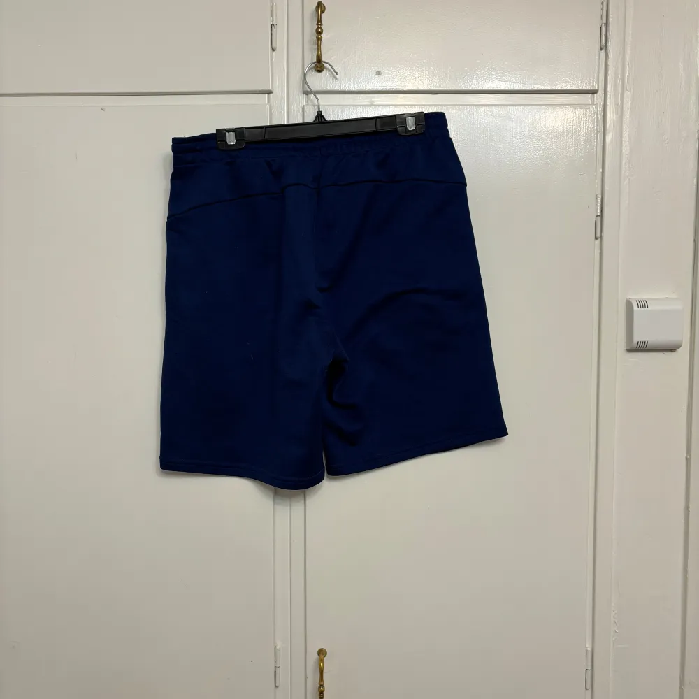 Säljer ett par mörkblå shorts från SOC i storlek M. De är perfekta för träning med en bekväm passform och elastisk midja. Materialet är mjukt och andas bra, vilket gör dem idealiska för varma dagar. De har praktiska fickor på sidorna för förvaring av småsaker.. Shorts.