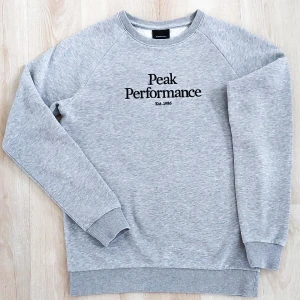 Peak Performance - Tröja  - Ljusgrå tröja från Peak Performance. Märkets logga sitter på bröstet och kommer med  ribbade muddar nedtill och vid ärmslut. Detta är ett klassiskt plagg. I mycket fint skick, har inga skador. Storlek:160 Kommer från djur och rökfritt hem. 