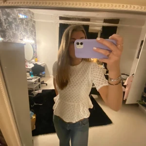 Vit spetsblus från Holly & Whyte - Säljer en söt vit spetsblus från Holly & Whyte by Lindex. Blusen har korta ärmar och en volangdetalj vid midjan. Perfekt för en stilren och elegant look.