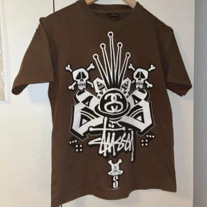 Stussy tshirt  - Cool brun t-shirt från Stussy med ett stort grafiskt tryck i vitt och svart på framsidan. Den är vintage och rare!