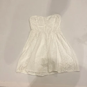 Vit axelbandslös klänning från Kimchi Blue - Söt vit axelbandslös klänning från Kimchi Blue med broderade detaljer. Perfekt för sommarens varma dagar. Klänningen har en kort längd och en smickrande passform.