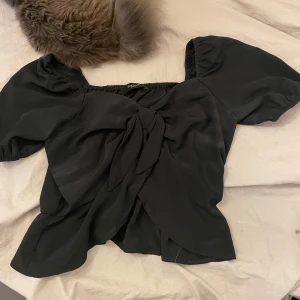 Svart blus med knyt - Snygg svart blus med puffiga kortärmar och knyt framtill. Perfekt för en stilren look.