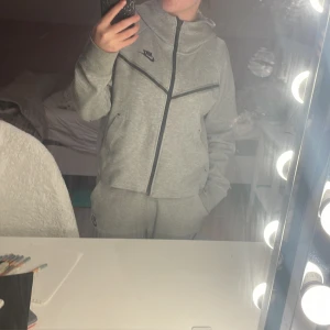 Grått Nike tech fleece set i dam. - Säljer detta set pågrund av att det kommer tyvärr ej till användning, som nytt. Tröjan är i storlek S och byxorna i XS. 