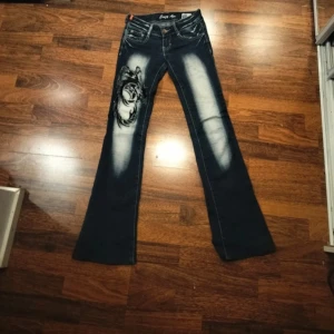 Mörkblå jeans med broderade detaljer - Snygga mörkblå jeans med unika broderade fjärilsdetaljer på bakfickorna och ett coolt mönster på benet. Jeansen har en bootcut-stil och är perfekta för dig som vill sticka ut. Crazy age! Priset går att diskutera🥰 passar någon med storlek 32 också :)