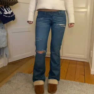 Blå bootcut jeans från Wrangler - Snygga blå bootcut jeans från Wrangler med slitna detaljer och låg midja❣️Jag på bilden är 170cm lång, Innerbenslängd: 81cm, midjemått 38,5cm❣️