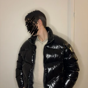 Svart pufferjacka från Armani Exchange - Snygg svart pufferjacka från Armani Exchange med hög krage och glansig finish. Jackan har en dragkedja framtill och är perfekt för kyligare dagar. Den har en modern look och passar bra till olika outfits.