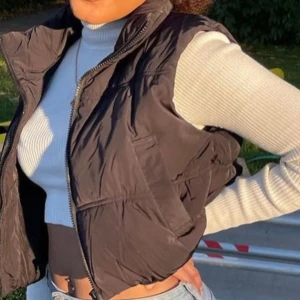 Svart croppad dunväst - Snygg svart dunväst med dragkedja, perfekt för lager-på-lager stil. Västen har en normal passform och är idealisk för kyligare dagar. Passar XS/S/M beroende på vilken passform du vill ha!