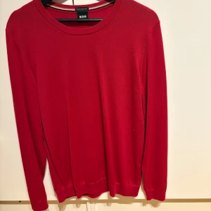 Röd tröja från BOSS - Snygg röd tröja från BOSS tillverkad av finaste italienska garn. Tröjan har en klassisk design med rund hals och långa ärmar. Perfekt för en stilren look.