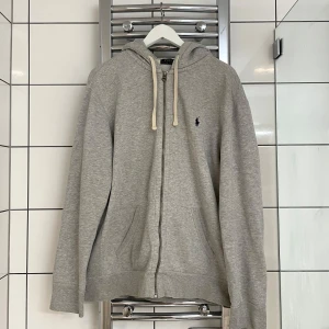 Grå hoodie från Polo Ralph Lauren - Säljer en stilren grå hoodie från Polo Ralph Lauren. Den har en dragkedja framtill och en klassisk logga på bröstet. Perfekt för både vardag och chill. Den är i bra skick och superbekväm att ha på sig. Nypris 1700 