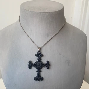 Svart gothiskt korshalsband - Snyggt svart korshalsband med detaljerad design. Korset hänger på en tunn silverfärgad kedja och har en elegant, antik look. Perfekt för att ge en stilfull touch till din outfit.