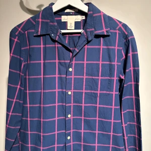 Blå och rosa rutig skjorta från H&M - Snygg blå skjorta med rosa rutmönster från H&M. Skjortan har långa ärmar och knappar framtill. Perfekt för en stilren look med en touch av färg.nypris 250