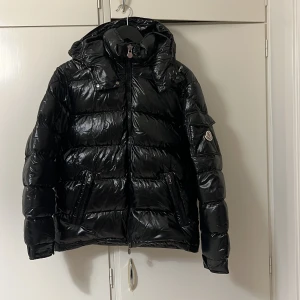 Svart Moncler Maya , Storlek 3 - Snygg svart pufferjacka från Moncler med glansig finish och dragkedja framtill. Jackan har en justerbar huva och är perfekt för kyliga dagar. Den är vadderad för extra värme och har Monclers logotyp på ärmen. Storlek 3 digital kvitto från Nk finns. Säljer den för att behöver storlek 4. Om de finns någon där ute som har storlek 4 som vill byta de e bara att skriva🫶🏻Flera bilder finns de e bara att skriva 
