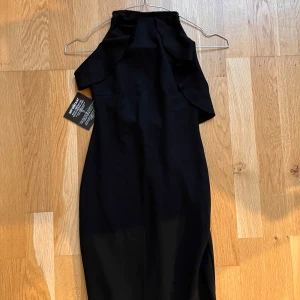 Helt ny svart festlig klänning med öppen från från Nelly - Snygg svart klänning från NLY Trend i storlek XS. Tillverkad i polyesterblandning med en elegant volangdetalj. Perfekt för en stilren look.