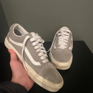 Gråa Vans - Tjena! Säljer ett par klassiska gråa Vans sneakers med vit sula och snörning. Skorna har den ikoniska sidoremsan i vitt och är tillverkade i mocka. Skorna är inte skadade och har ingen defekt de är bara lite smutsiga. Perfekta för en avslappnad stil. Hör av er vid minsta fundering!